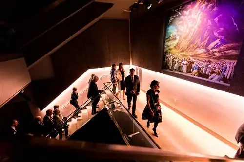 Люди поднимаются по освещенной пурпуром лестнице в Музее Холокоста и прав человека в Далласе.