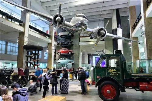 Небольшой самолет подвешен к потолку огромного музейного зала, заполненного различными видами транспорта.