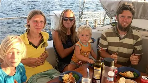 Семья из двух взрослых и троих детей обедает на палубе своей парусной яхты.