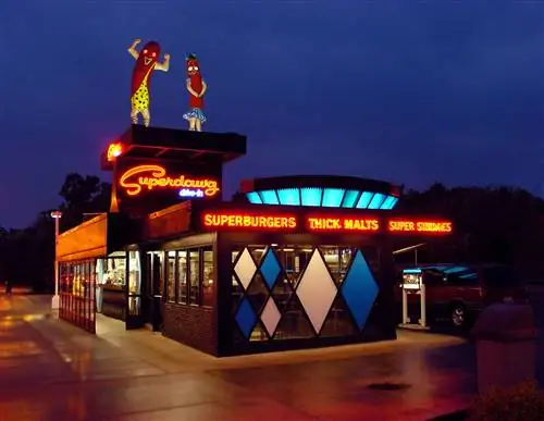 Ночное фото экстерьера SuperDawg Drive-In. На крыше ресторана стоит пара больших хот-догов из стекловолокна.