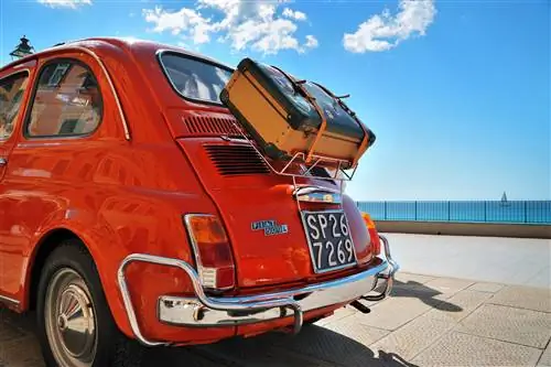 Небольшой старый автомобиль Fiat 500L с чемоданом, привязанным к его задней части. Небольшой старый автомобиль Fiat 500L с чемоданом, привязанным к его задней части.