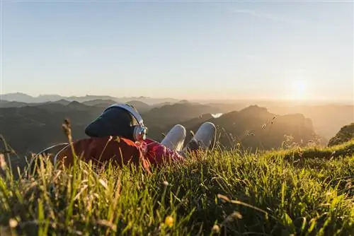 Путешественник лежит в траве, отдыхает и слушает музыку в наушниках