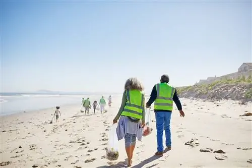 Добровольцы в светоотражающих жилетах убирают пляж с белым песком в солнечный день.