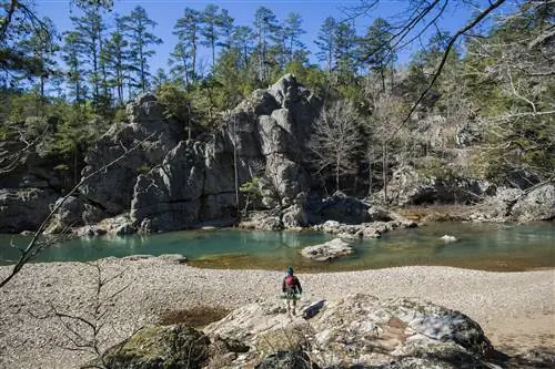 Путешественник с полным туристическим снаряжением идет к большим скальным образованиям и реке в горах Уашита в западно-центральном Арканзасе.