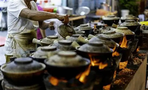 Уличный торговец готовит куриный рис в глиняном горшочке на ночном рынке в Куала-Лумпуре.