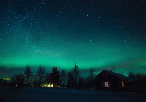 Северное сияние (Aurora Borealis) над заснеженным коттеджем в деревне Лапландия. Финляндия