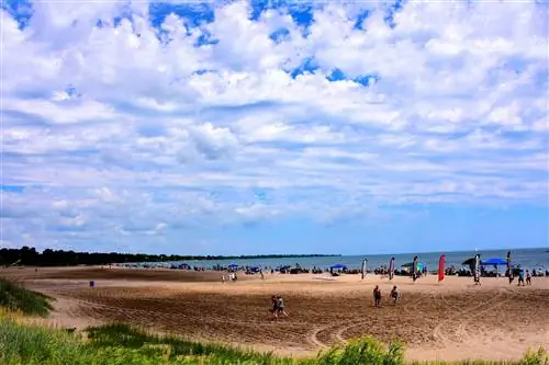 Многие люди наслаждаются пляжными развлечениями на Северном пляже в прекрасный летний день с облачным небом над прохладными водами озера Мичиган.