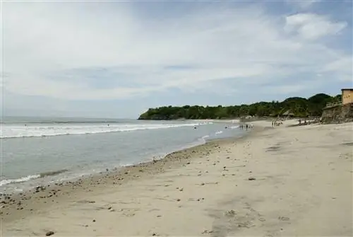 Широкий угловой вид на пляж Эль-Пальмар в Панаме. Пляж песчаный и плавно спускается в ласковое море. Несколько семей стоят на песке вдалеке.
