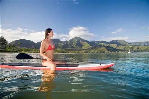 Женщина сидит на доске для серфинга в бухте Ханалей, курорт, Кауаи, Гавайи, США