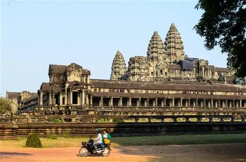 Мотоцикл с двумя людьми проезжает по грунтовой дороге у храма в Ангкор-Ват, Сием-Рип, Камбоджа, Юго-Восточная Азия.