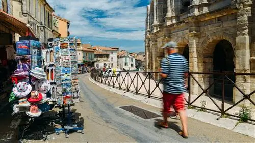 Туристы проходят мимо сувенирных магазинов, торгующих открытками и календарями, рядом с Ареной д'Арль, римским амфитеатром.