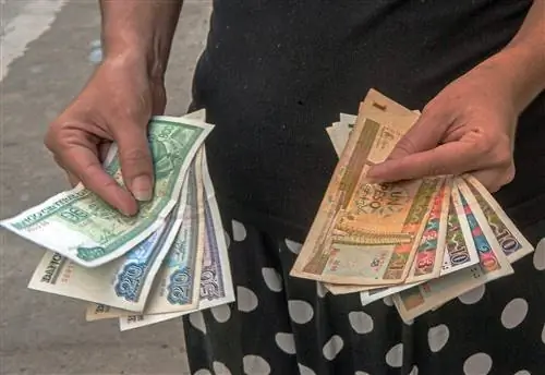 Кубинец показывает кубок кубинских песо (левая рука) и конвертируемых песо CUC (правая рука),