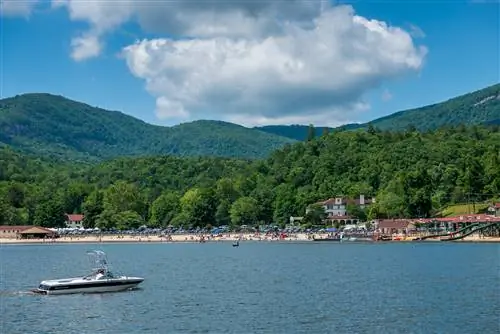 Пляж на озере Люр, Северная Каролина, ранним днем. Люди на пляже и лодка на переднем плане. Вид на горы на заднем плане.