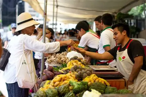 Женщина в белой рубашке и шляпе передает деньги продавцу овощей на рынке в Милафлорес, Лима, Перу.