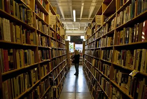 Женщина заглядывает в книгу в конце длинного ряда книжных полок на первом этаже Книжного города Пауэлла в Портленде, штат Орегон.