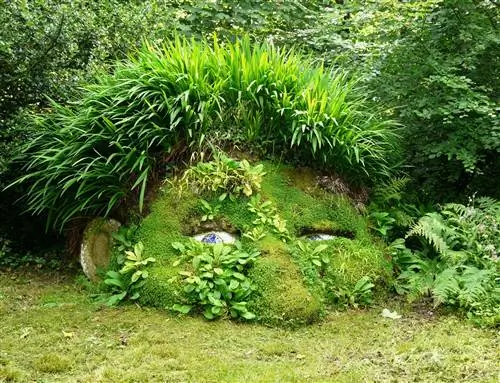 Скульптура в виде наполовину зарытой головы великана, покрытой растениями.