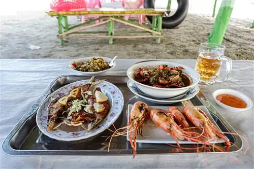 Поднос с несколькими блюдами из морепродуктов, в том числе свежими креветками и крабовым карри, стоит на столе на песке пляжа Але-Ва.