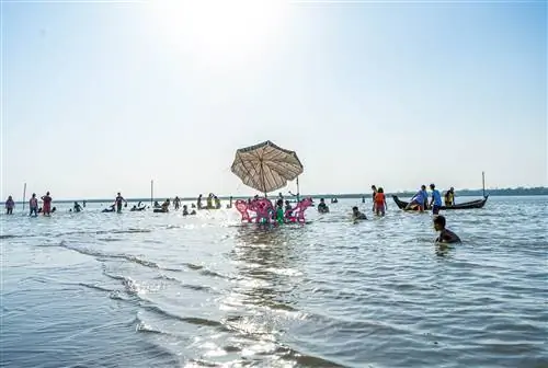 Стол и три стула медленно погружаются в воду приливом, омывающим пляж в Мьянме. Многие люди гребут на мелководье.
