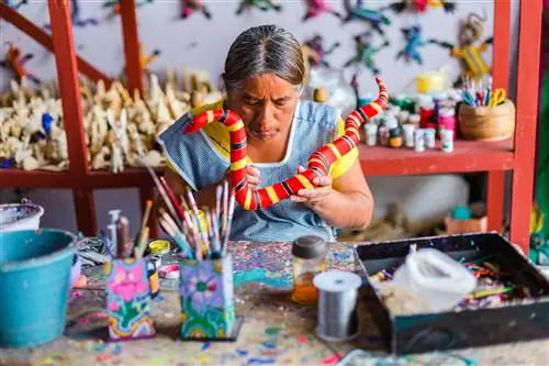 Художник рисует красочную скульптуру алебрихе из резного дерева в студии в Сан-Мартин-Тилькахете.