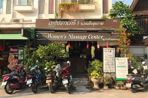 Перед магазином с большой вывеской на тайском и английском языках с надписью «Центр женского массажа» бывших заключенных. Перед магазином припарковано пять мотоциклов.