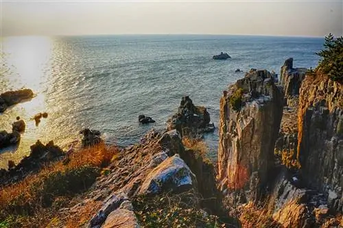 Вид на побережье с видом на море на закате. Скалы на побережье зазубренные, а некоторые образуют столбообразные структуры.