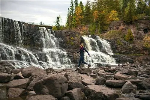 Женщина прыгает по скалам перед водопадом