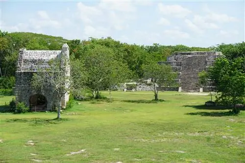Два каменных здания на поле зеленой травы с лиственными деревьями
