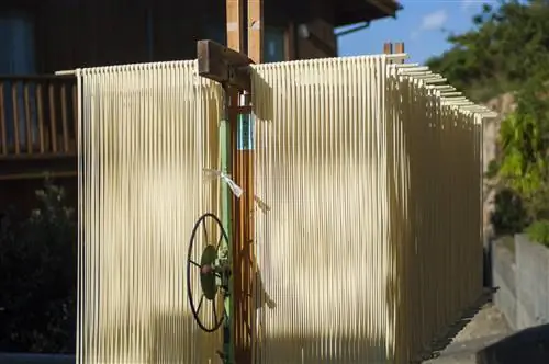 Длинные пряди лапши сёдосима сомэн свисают со стоек снаружи, чтобы высохнуть на солнце. Шторки лапши выглядят почти как сарай из деревянных реек они такие длинные и стойки уходят так глубоко, с металлическим колесом в центре рамы для регулировки стоек