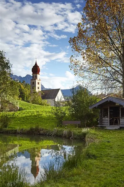 Красный купол церкви Сант-Освальдо отражается в горном пруду.