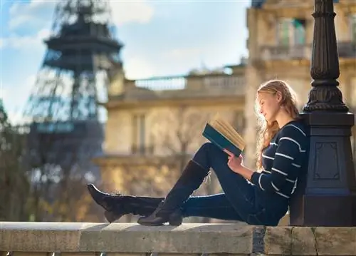 Женщина сидит на стене в Париже и читает книгу. На заднем плане видна Эйфелева башня.