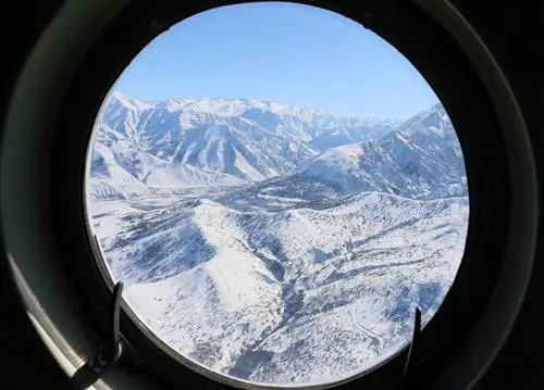 Вид на красивые белые горы через круглое окно вертолета.