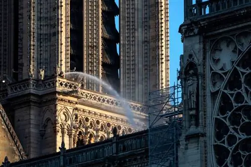 Пожарный поливает из шланга часть собора Нотр-Дам на следующий день после сильного пожара, уничтожившего его крышу.