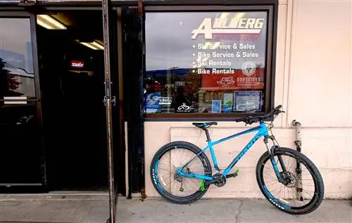 Синий горный велосипед стоит у входа в Arlberg Sports в Уэнатчи, штат Вашингтон, название которого написано кремовыми буквами на окне над велосипедом вместе с информацией об аренде лыж и велосипедов.