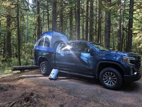 Темно-синий грузовик GMC Sierra 2019 года с ярко-синим и серым тентом, установленным на кузове, стоит в зеленом лесу в штате Вашингтон.