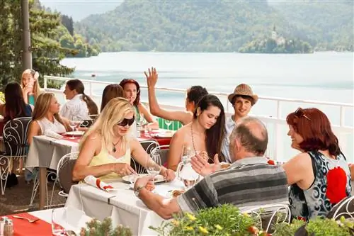 Люди едят на террасе с видом на озеро Блед в солнечный день
