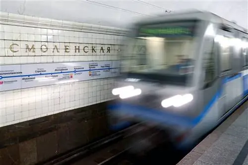 Размытый поезд, проезжающий на скорости через станцию с плиточной стеной и путеводителем по станции.