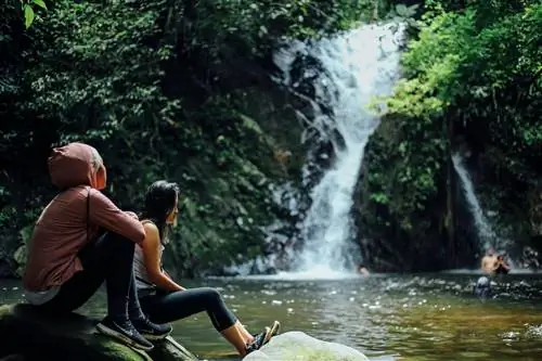 Две женщины сидят у бассейна возле водопада в джунглях