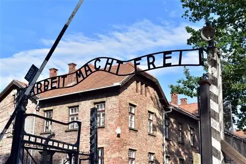 Железные буквы над воротами означают Arbeit Macht Frei (работа освобождает). На заднем плане двухэтажное здание из красного кирпича.