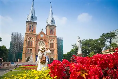 Женщина стоит лицом к огромному зданию собора из красного кирпича с двумя башнями-близнецами.