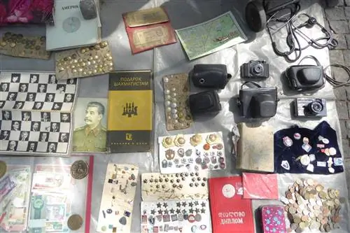На циновке на рынке выставлено множество различных предметов, в том числе монеты, значки и книги советской эпохи.