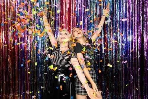 Две женщины позируют на фоне разноцветных серпантинов