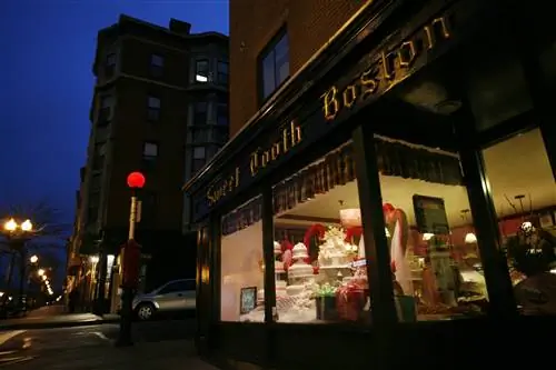 Внешний вид Sweet Tooth Бостон ночью. Золотые надписи Sweet Tooth Boston отражали уличные фонари. В витрине можно увидеть большие торты и другие украшения.