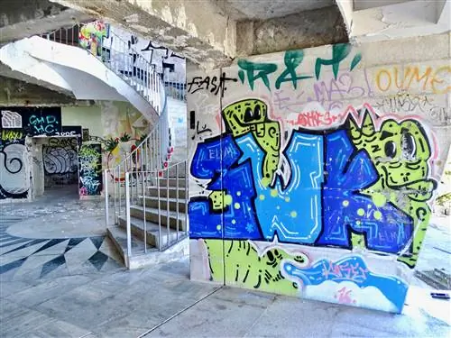 Бетонная винтовая лестница, окаймленная стенами с граффити, в Miradouro Panoramico de Monsanto, Лиссабон.