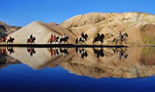 Десяток человек верхом на лошадях пробираются по зеркально-спокойному озеру, и их отражения хорошо видны; за ними какие-то бесплодные, желтовато-коричневые холмы.