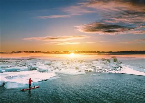 Одинокий гребец в экипировке для выживания пробирается вдоль края ледника в море, а солнце садится за облака вдалеке.