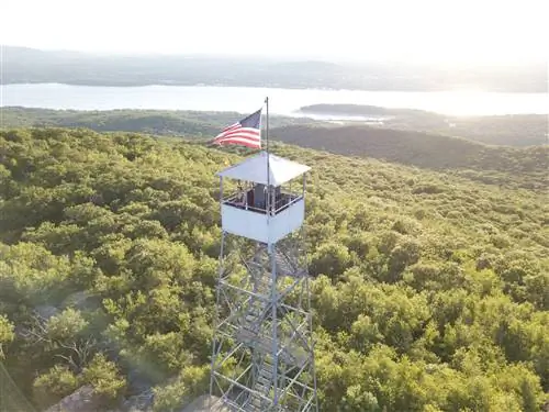 Женщина в башне с американским флагом, смотрящая на реку Гудзон, зелень и горы