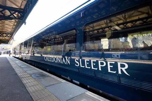 Королевский синий поезд стоит на станции с белым логотипом Caledonian Sleeper сбоку; Удивительные путешествия на поезде