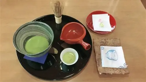 Чай матча подается в Такуми-но Яката на черном подносе. Чай находится в маленькой зеленой миске, рядом с красной насадкой, деревянным венчиком и маленькой чашкой.