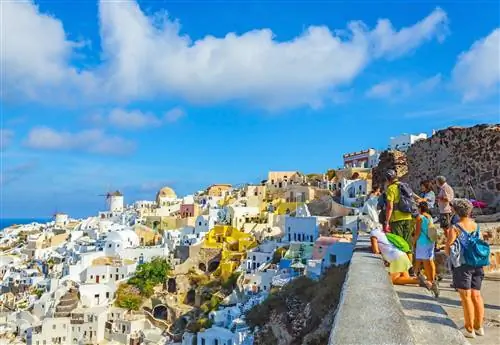 Небольшая группа туристов собирается, чтобы полюбоваться видом на белые здания, встроенные в скалы на Санторини.