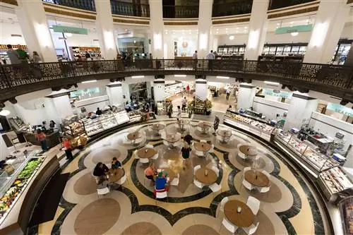 Глядя вниз с галереи на столовую внутри Heinen's Fine Foods; есть несколько круглых столов, а круглое пространство уставлено стеклянными шкафами с едой.